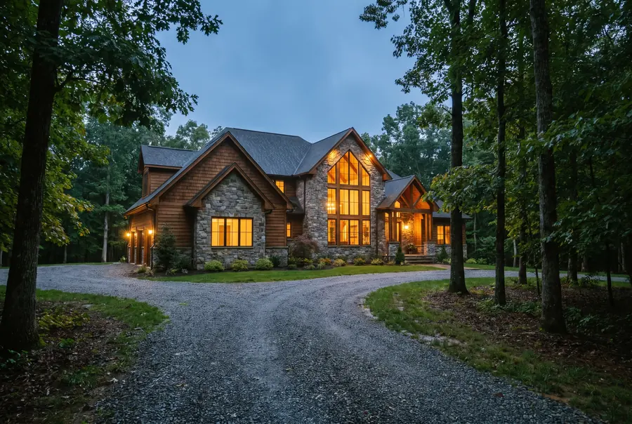 A large custom built American home with a stone and cedar facade and tall lit windows at blue hour.